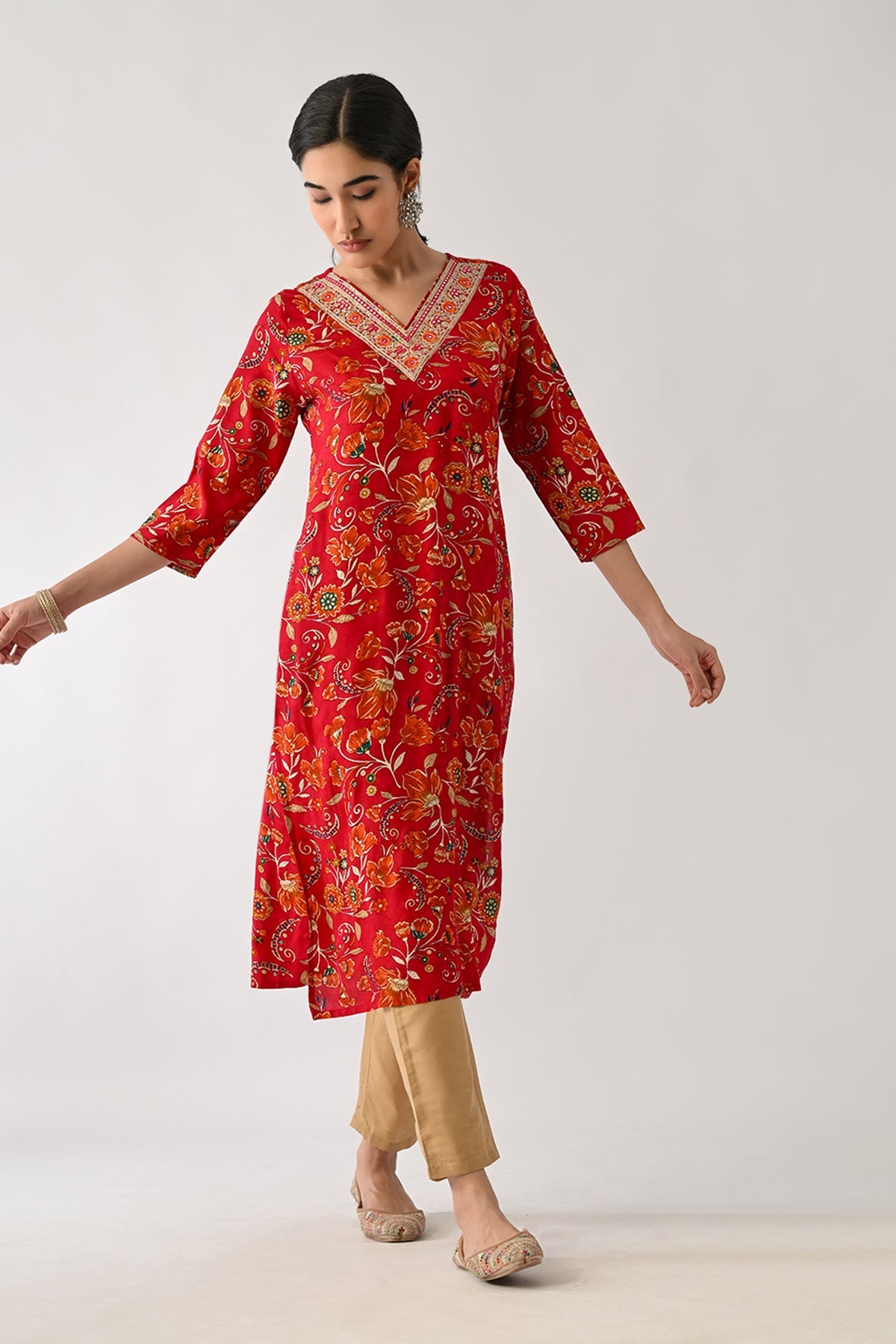 Woman wearing a red floral kurta with beige pants on a white background