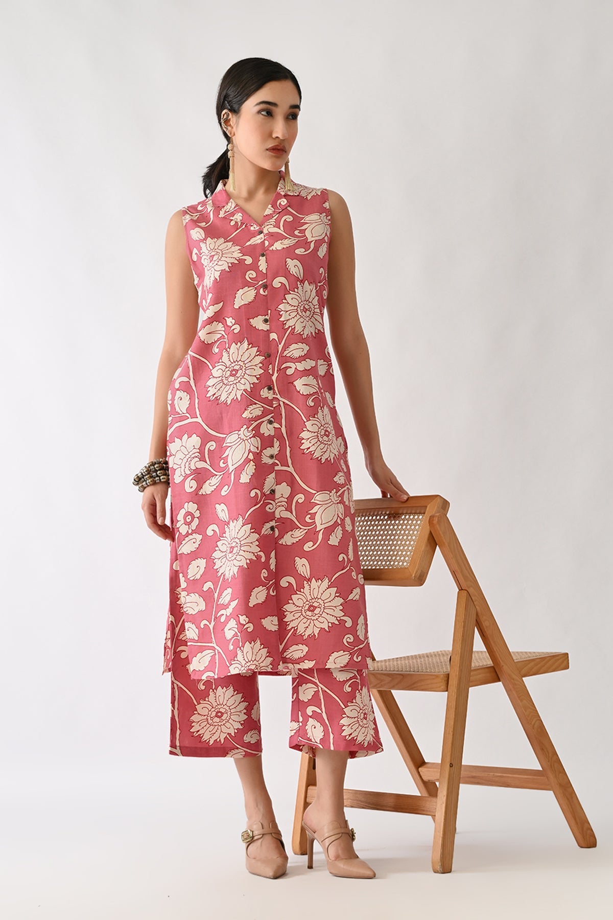 Woman wearing a pink floral dress standing next to a wooden chair on a white background