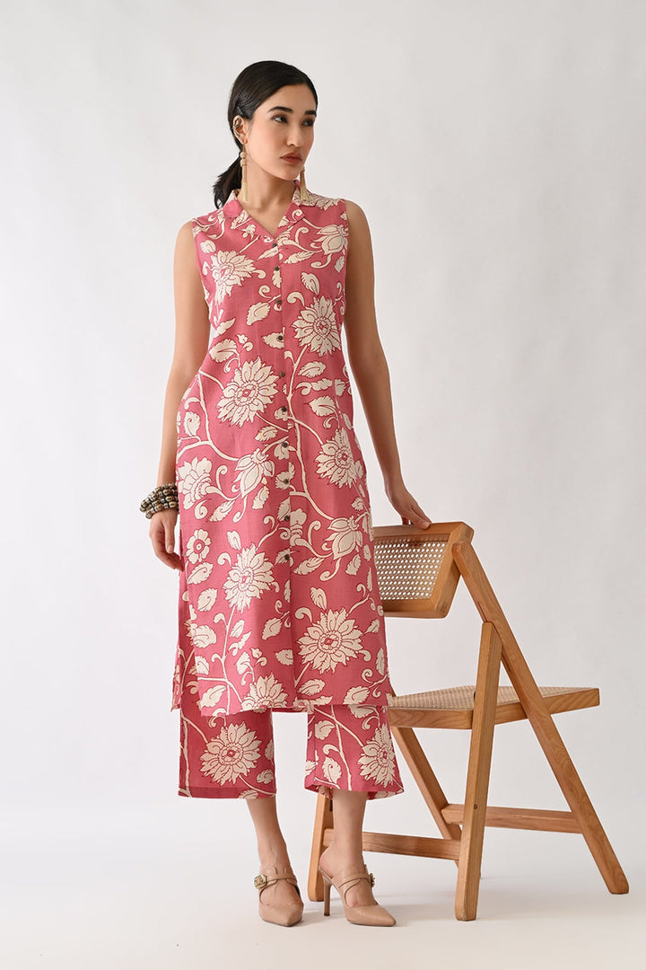 Woman wearing a pink floral dress standing next to a wooden chair on a white background