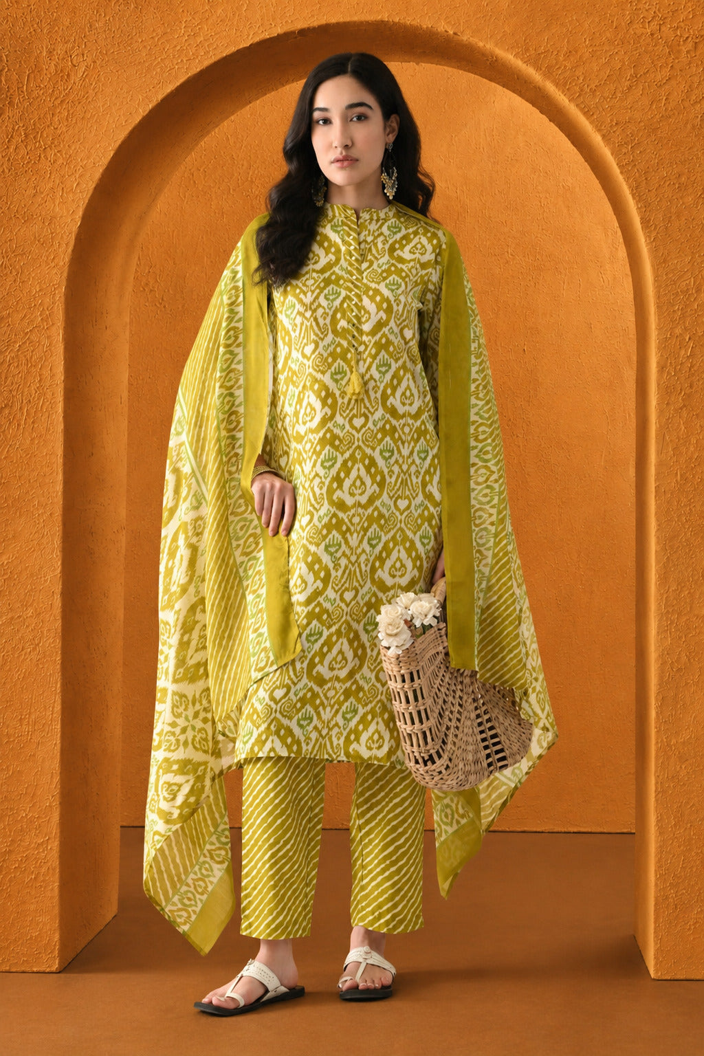 Woman in a yellow and white patterned outfit standing in front of an orange archway.