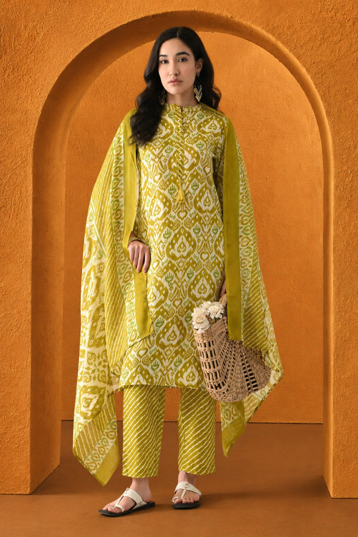 Woman in a yellow and white patterned outfit standing in front of an orange archway.