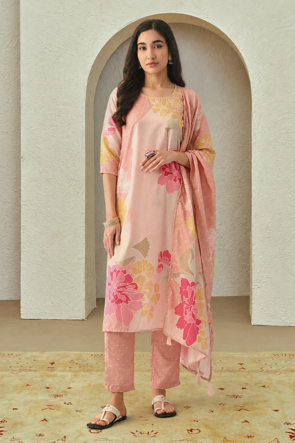 Woman wearing a pink floral outfit standing in front of an archway.